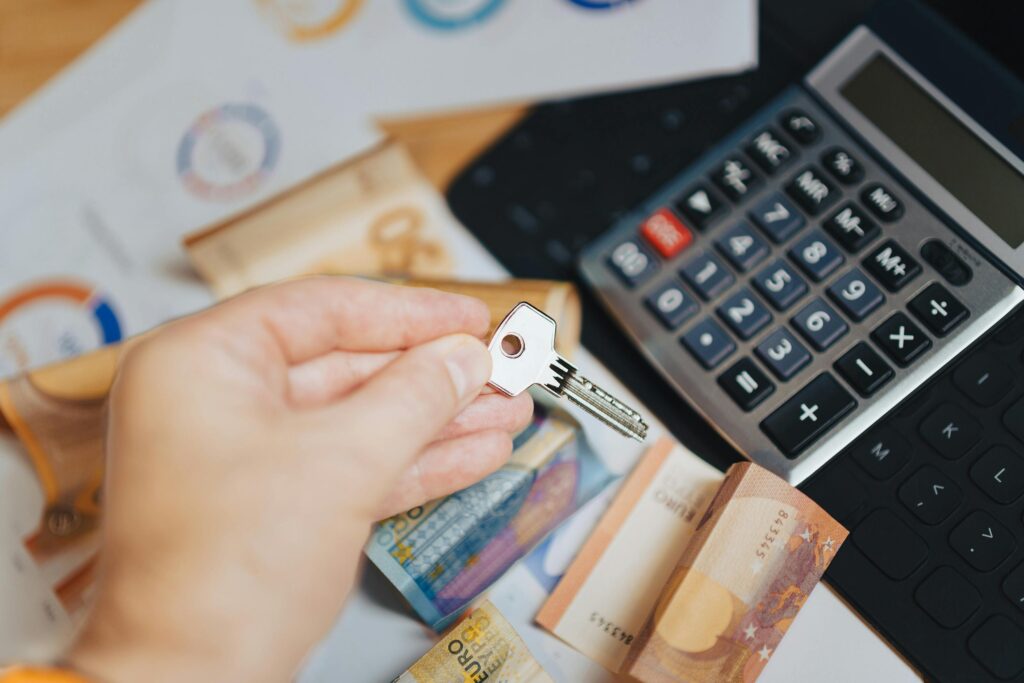 A hand holding a key above some money and a calculator.