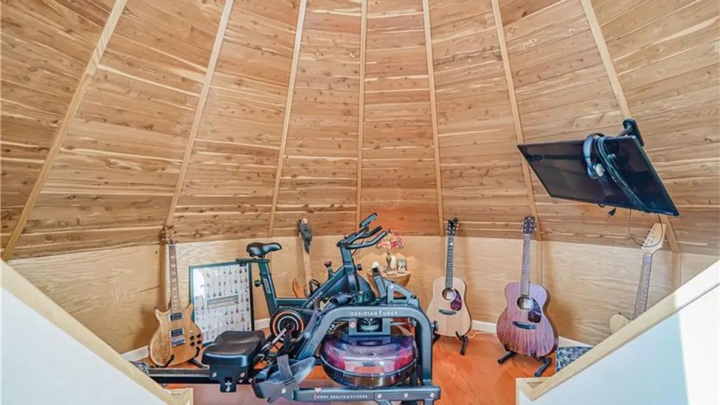 Wooden dome-shaped room with a rowing machine and guitars.