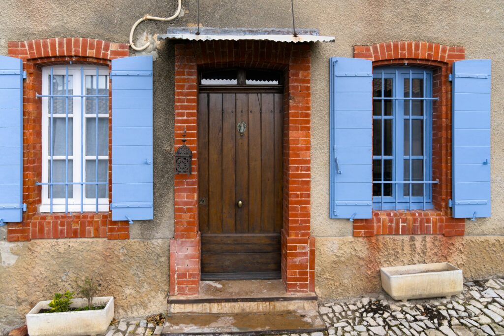 A door flanked by two windows with bricks and blue shutters.