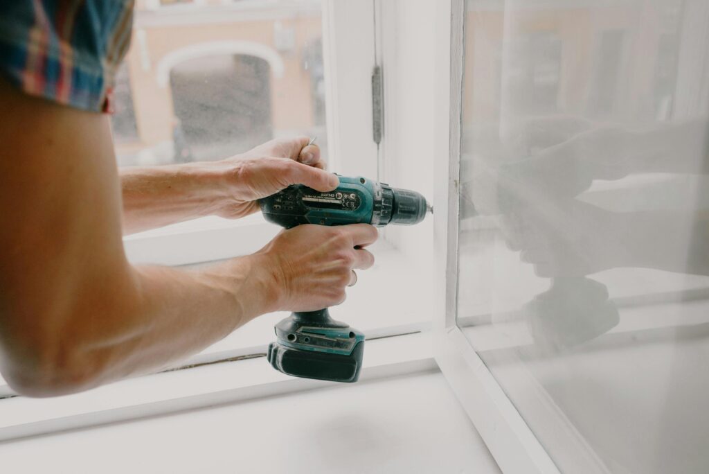 A worker using a cordless screwdriver to replace a window.