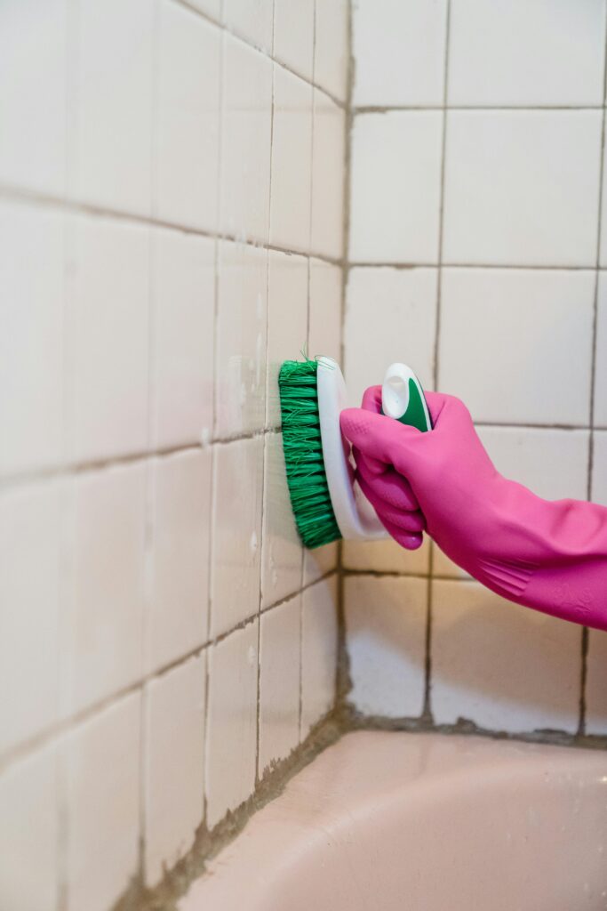 A gloved hand holding a brush, cleaning a tiled wall.