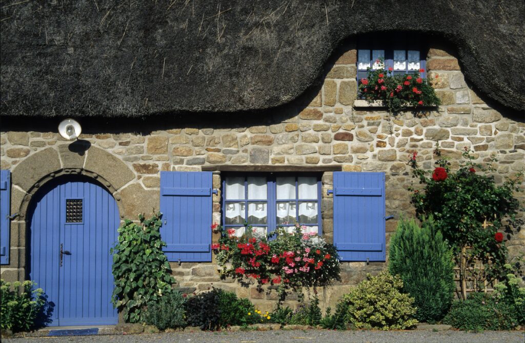 Façade of a cottage with a blue door and window shutters.