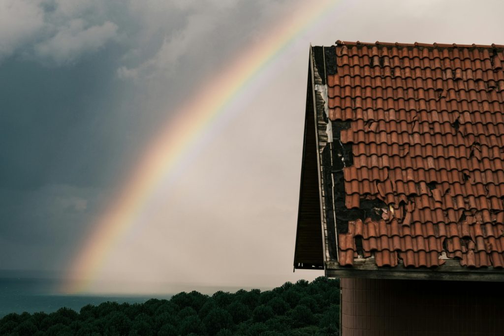 A damaged roof with a rainbow in the backdrop.