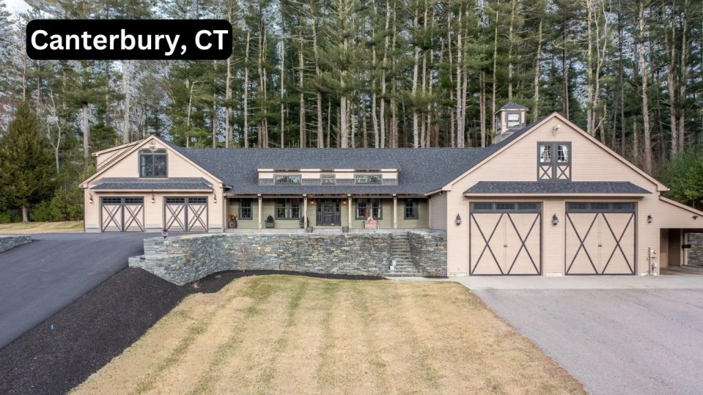 A beautiful single-family home in Canterbury, CT, featuring barn-style garage doors, a covered porch, and a scenic wooded backdrop.