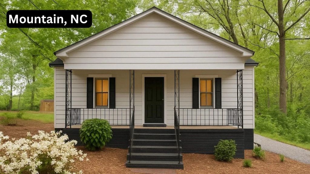 Cozy white cottage with green door and porch set in a wooded area.