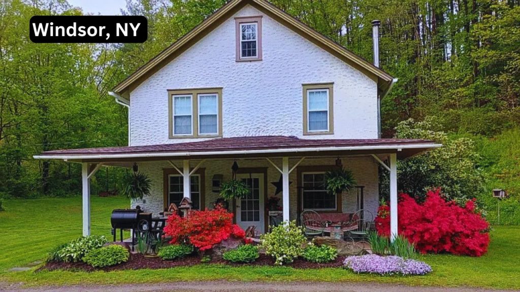 White farmhouse-style home with porch and colorful garden in Windsor, NY.