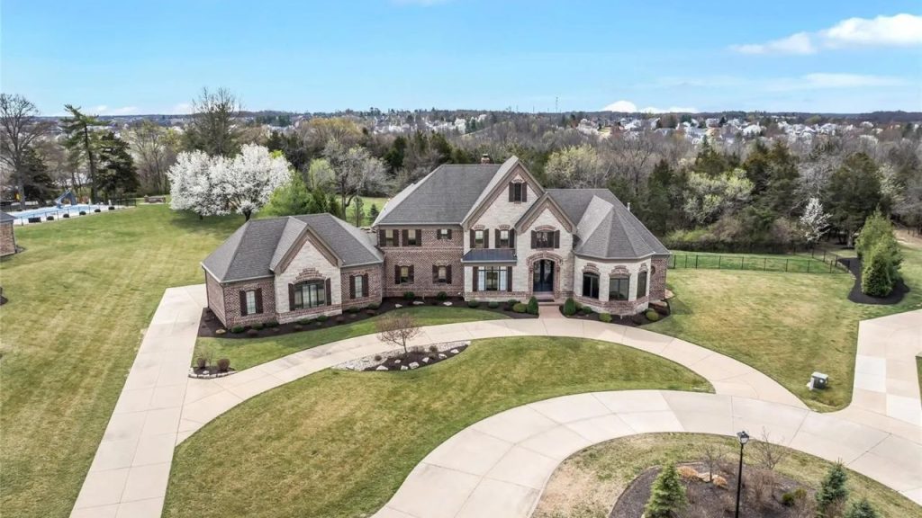 A stately brick and stone estate with a circular driveway, surrounded by lush greenery.