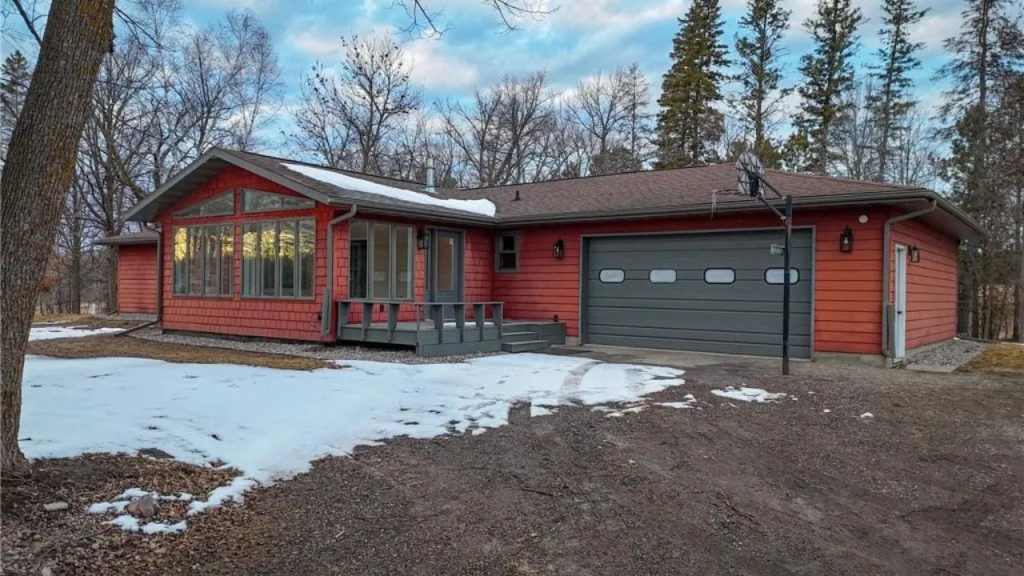 A red single-family home with a front porch and garage surrounded by trees and light snow.