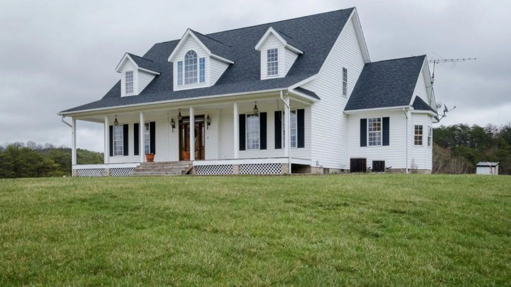 White farmhouse with a wraparound porch on a large open field.
