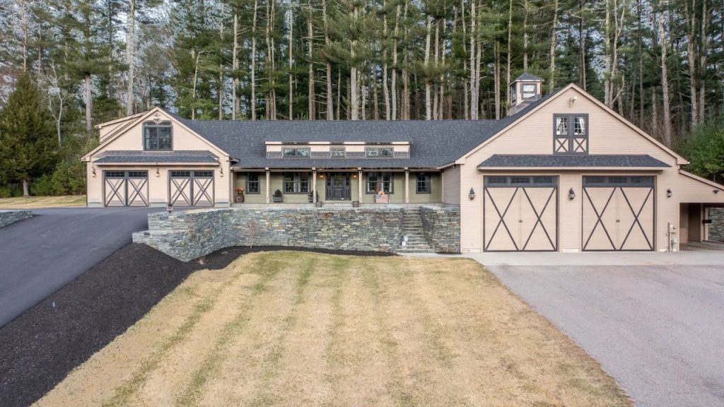 Barn-style home with a large garage, stone retaining wall, and wooded backdrop.