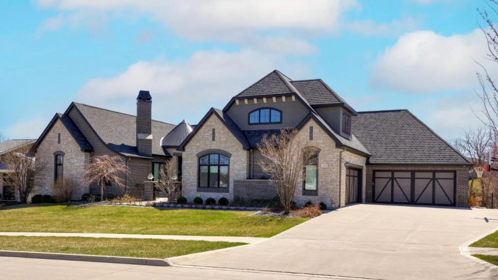 Elegant stone and brick home with gabled roof, large windows, and a spacious driveway in Waukee, Iowa.