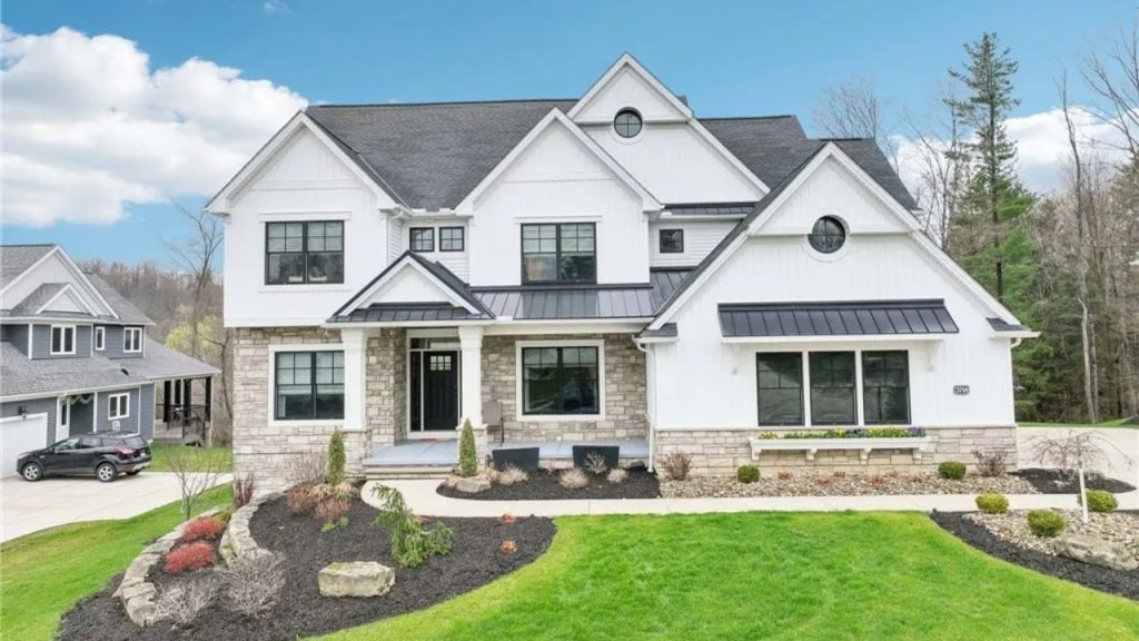 A charming colonial modern home with white siding, black roof, and stone accents, featuring large windows and a landscaped lawn.