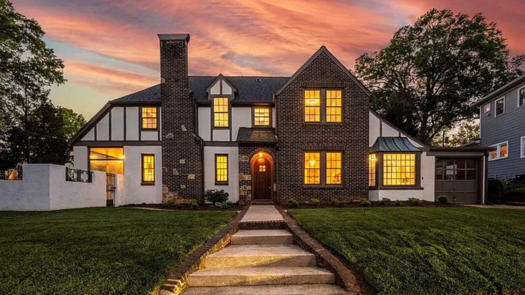A beautiful colonial-style home with a brick exterior, glowing windows, and a stone pathway at sunset.