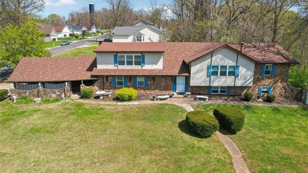 A charming colonial-style home with a modern twist, featuring a stone base, blue shutters, and a sprawling green lawn, set in a leafy suburban neighborhood.