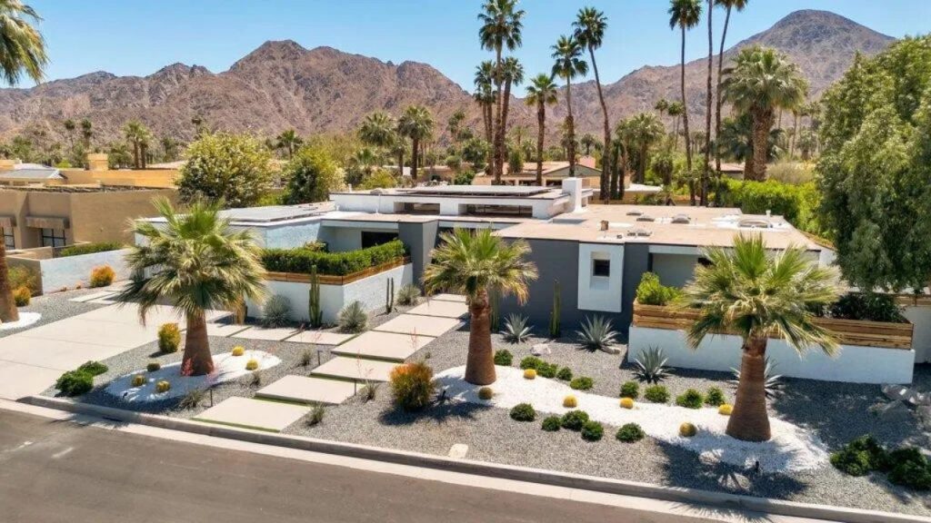 Modern desert home with palm trees, cacti, and a mountain backdrop.