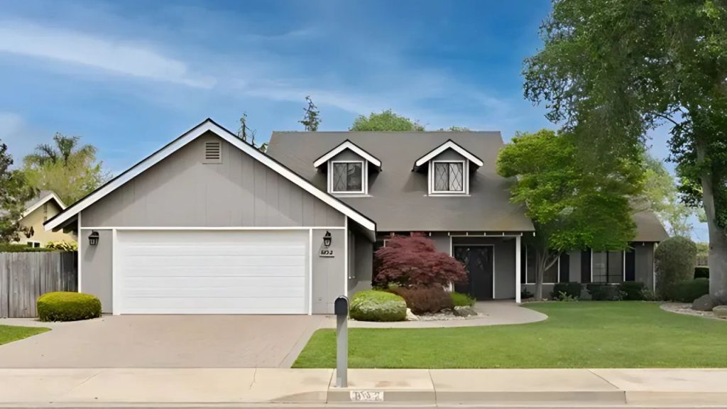 Neatly designed gray home with dormers, porch, and front yard landscaping.