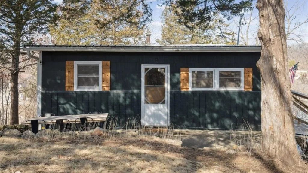 A rustic cabin with dark green siding, wooden shutters, and a peaceful wooded setting in Delhi, IA.