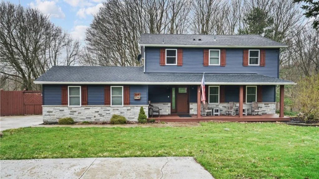 Two-story colonial-style house with navy siding, red shutters, and a stone base.






