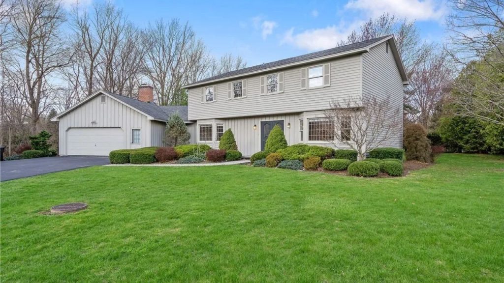 Two-story Colonial-style home with neutral siding, large front lawn, and attached garage.