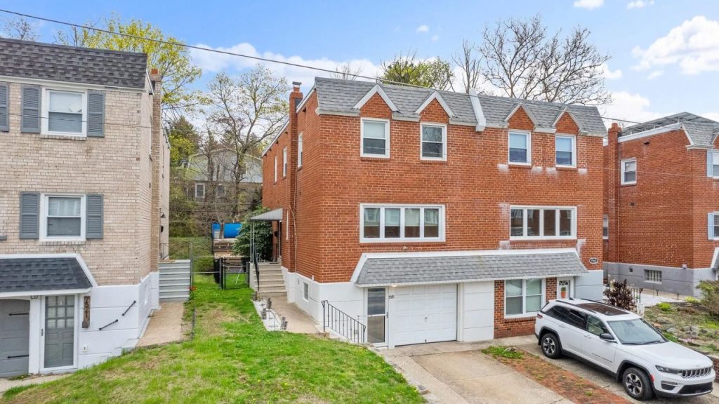 Red brick Colonial-style rowhome with pitched gables and a one-car garage.