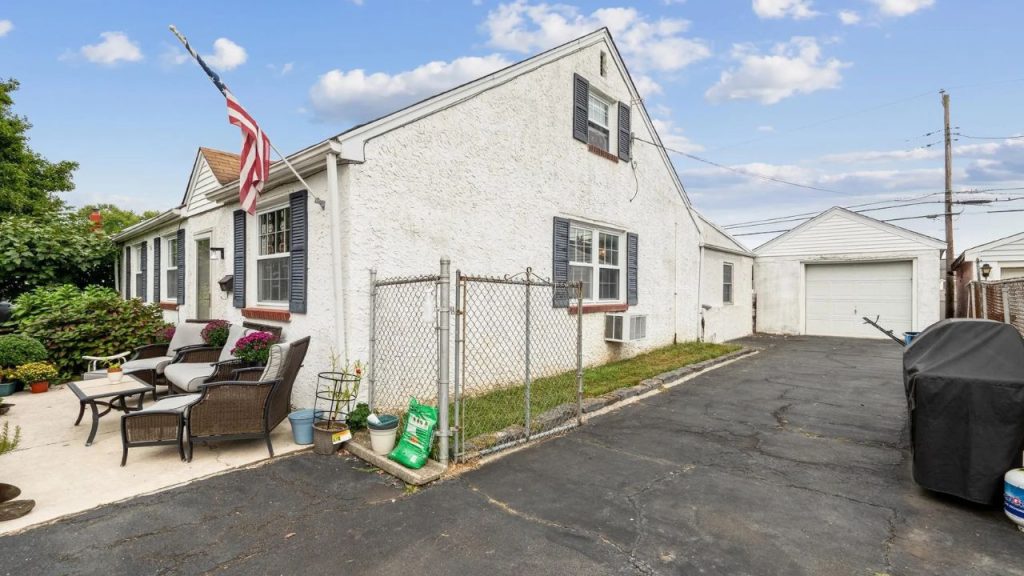 Cape Cod home with stucco exterior, front patio, and detached garage.