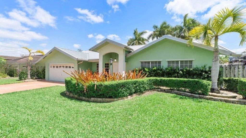 Bright green home with a tropical garden and palm trees under a blue sky.
