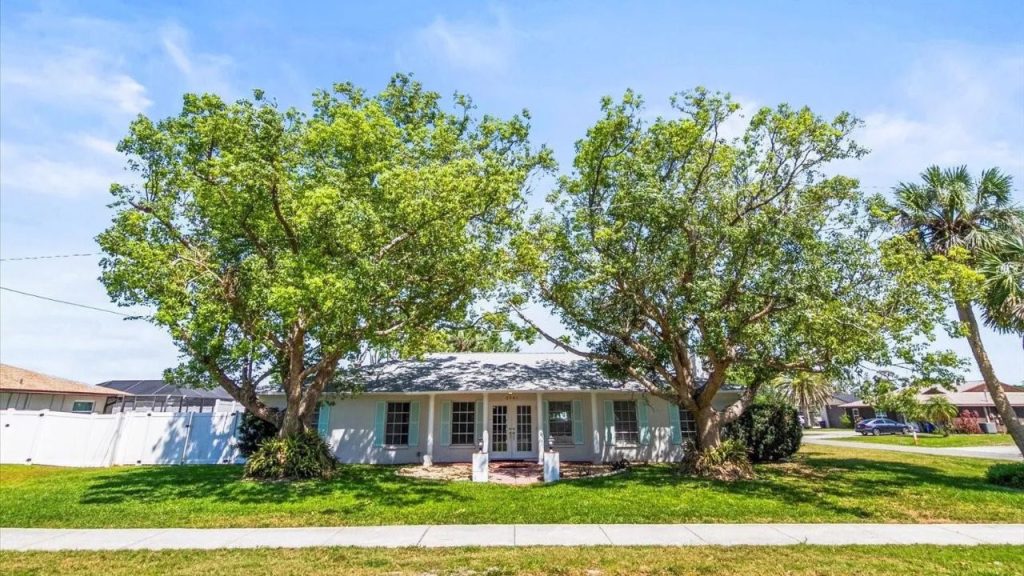 Front yard with two large trees and a cozy white home in Venice, Florida.