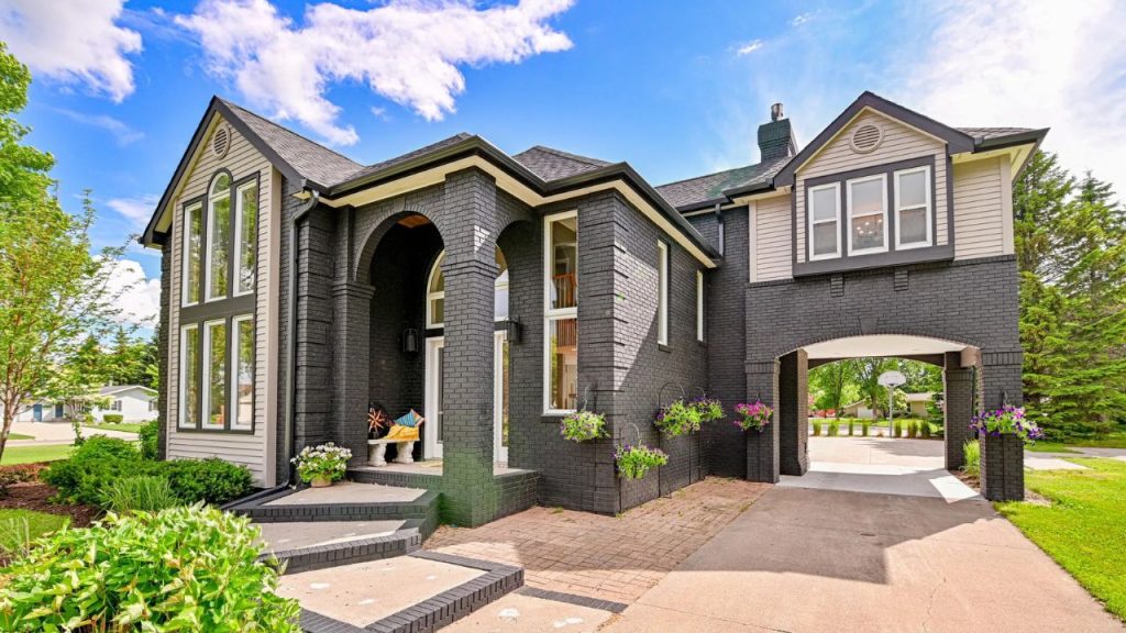 Arched entryway and bold black brick exterior with flowers and a driveway.