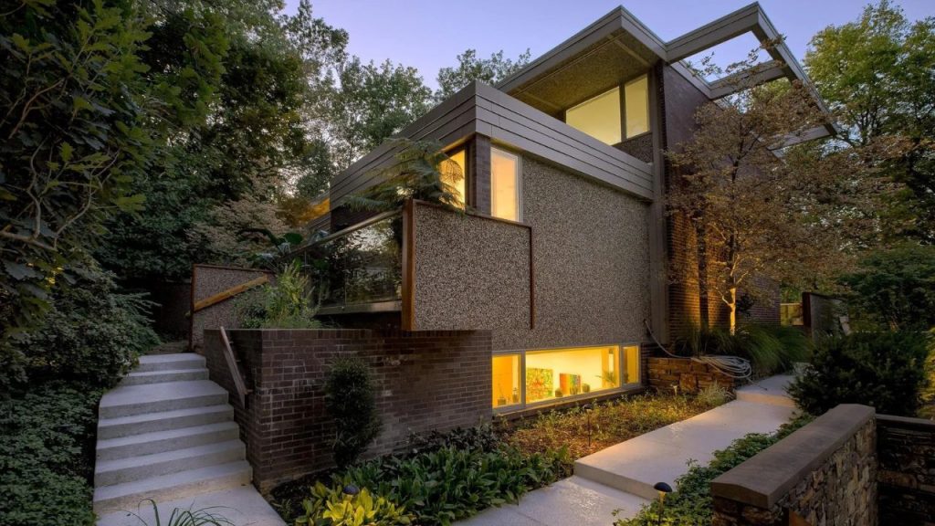 Modern multi-level home surrounded by trees and glowing softly at dusk.