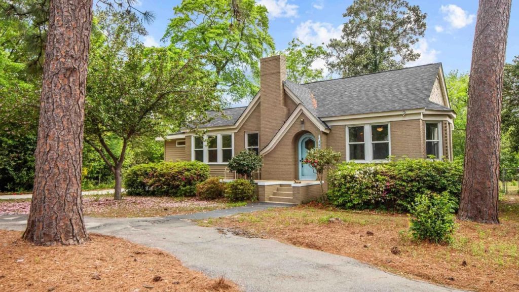 Tan brick home with arched front entry and tall trees surrounding the yard.