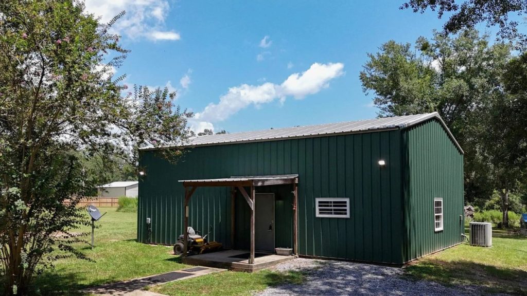Green metal shed with a small porch in a grassy backyard.