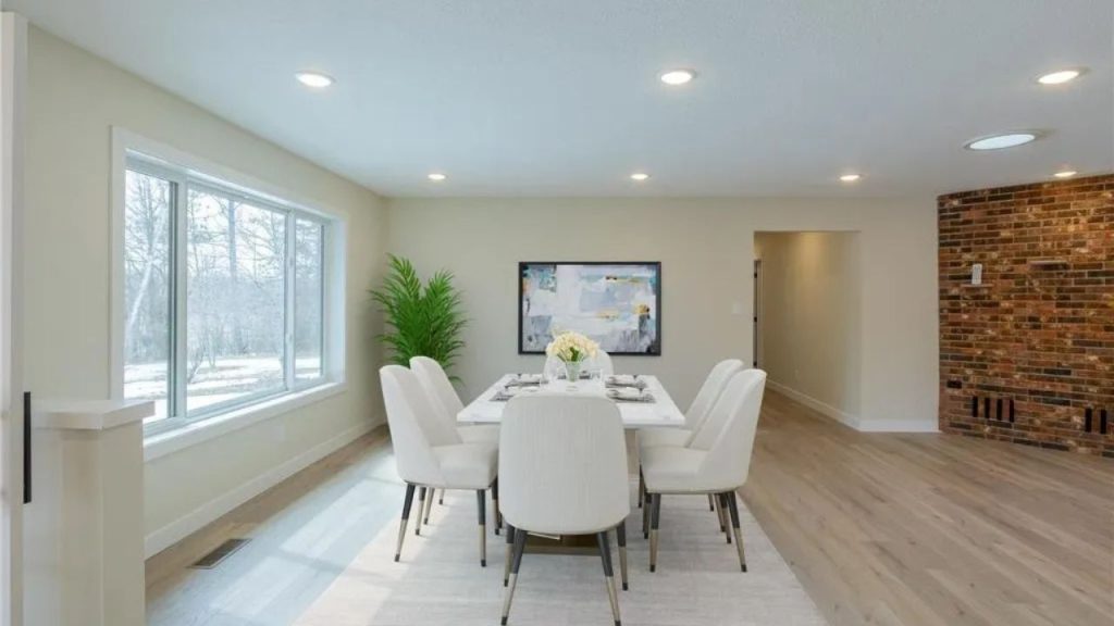 Bright dining area with white chairs, large window, and brick accent wall.