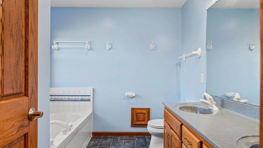 Blue bathroom with double sinks, bathtub, and wood cabinets.