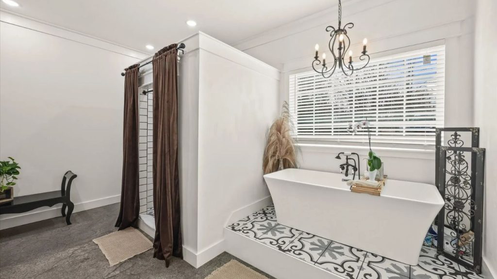 Elegant bathroom with a freestanding tub, vintage chandelier, and patterned tile flooring.
