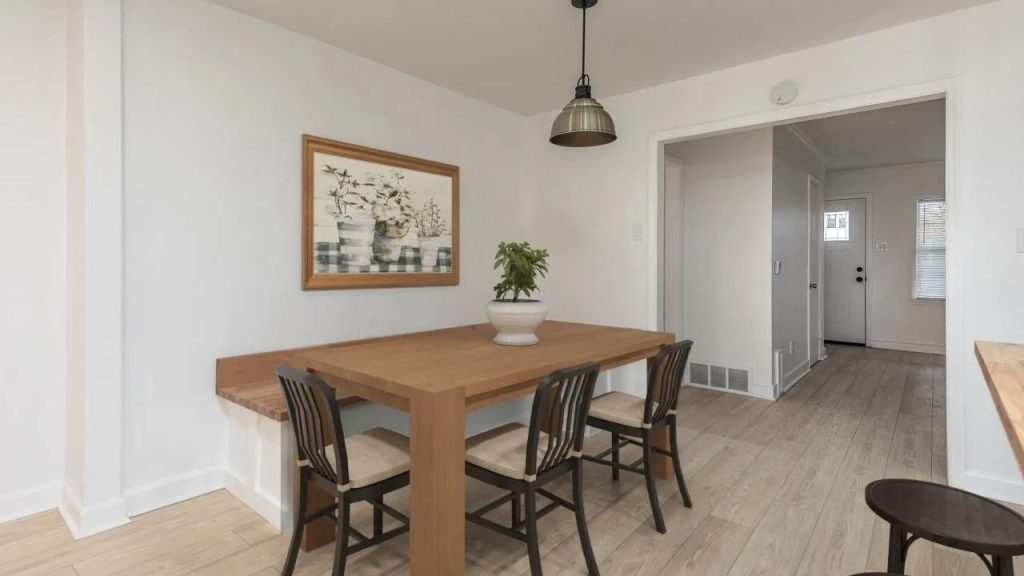 A cozy dining area with a wooden table, chairs, built-in bench, and floral artwork under a pendant light.