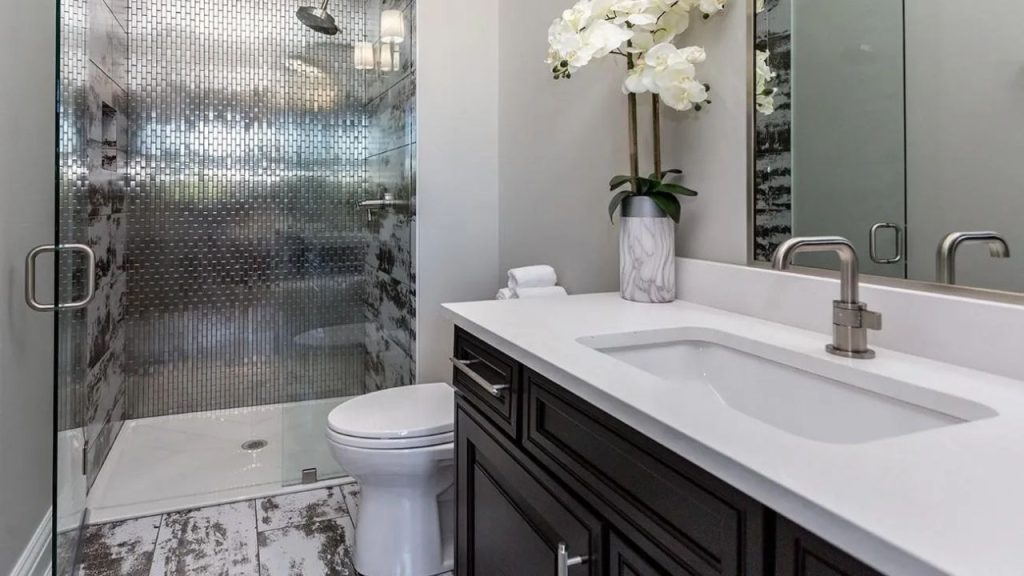 A serene bathroom with metallic-tiled shower, marble vanity, white orchids, and large windows, offering a calm and stylish escape.
