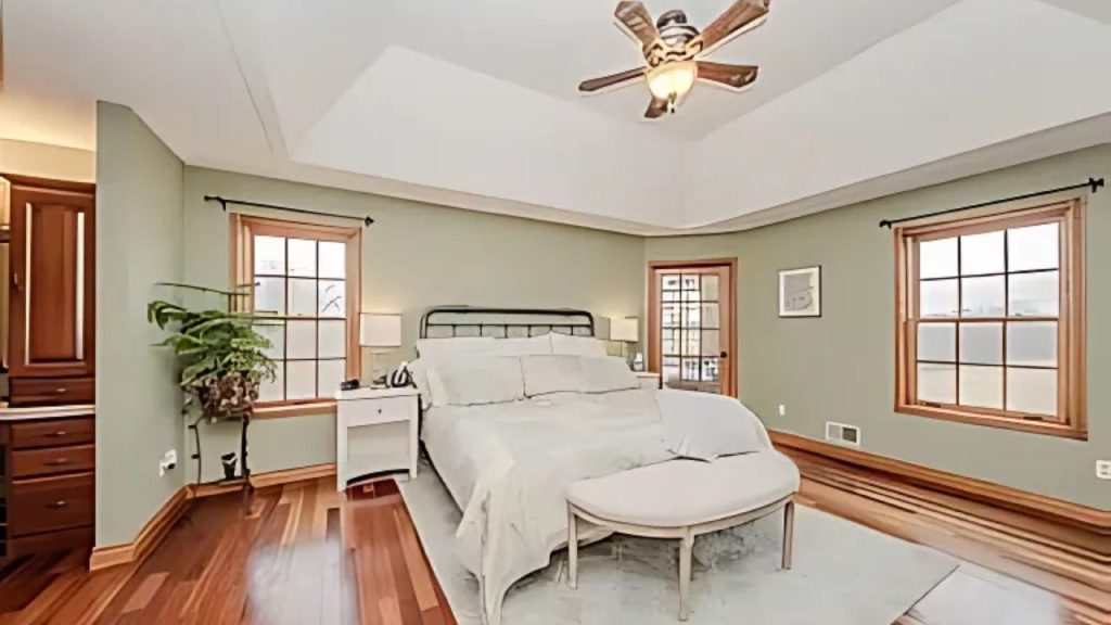 A calm master bedroom with a tray ceiling, hardwood floors, and a cozy bench.