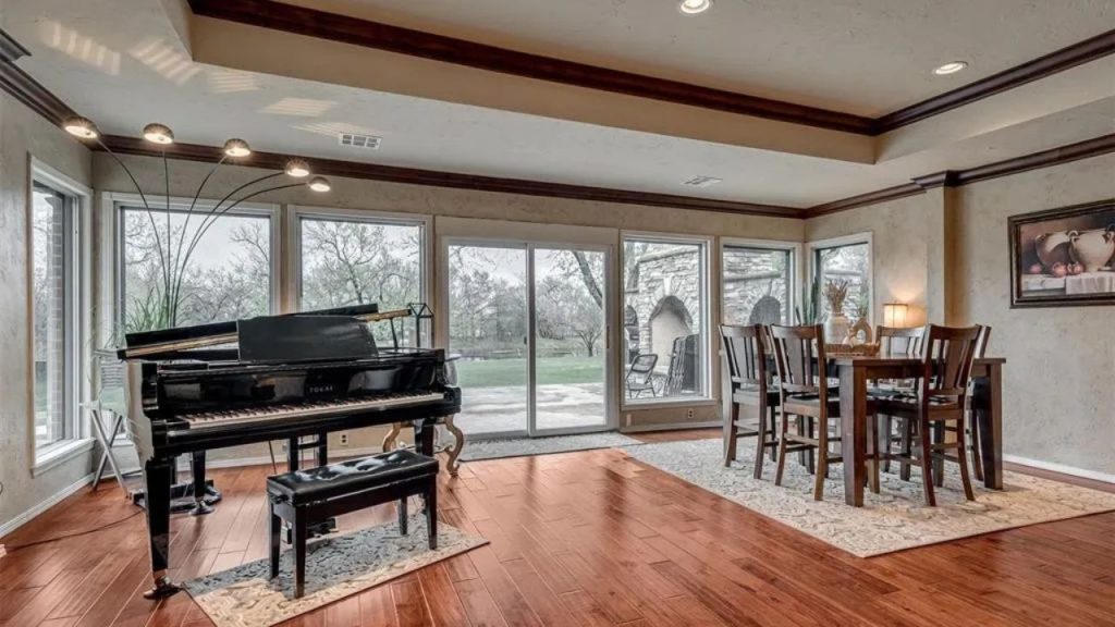 Bright dining room with a piano, wooden table, and large windows, featuring hardwood floors and a view of the backyard.