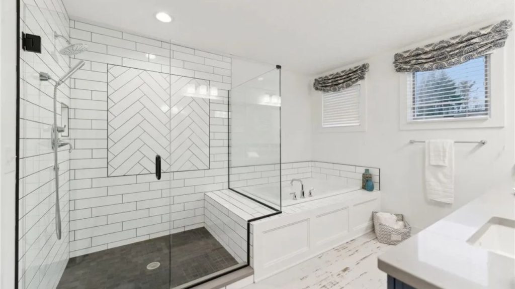 A serene bathroom with a glass shower, soaking tub, and white tiles near large windows.