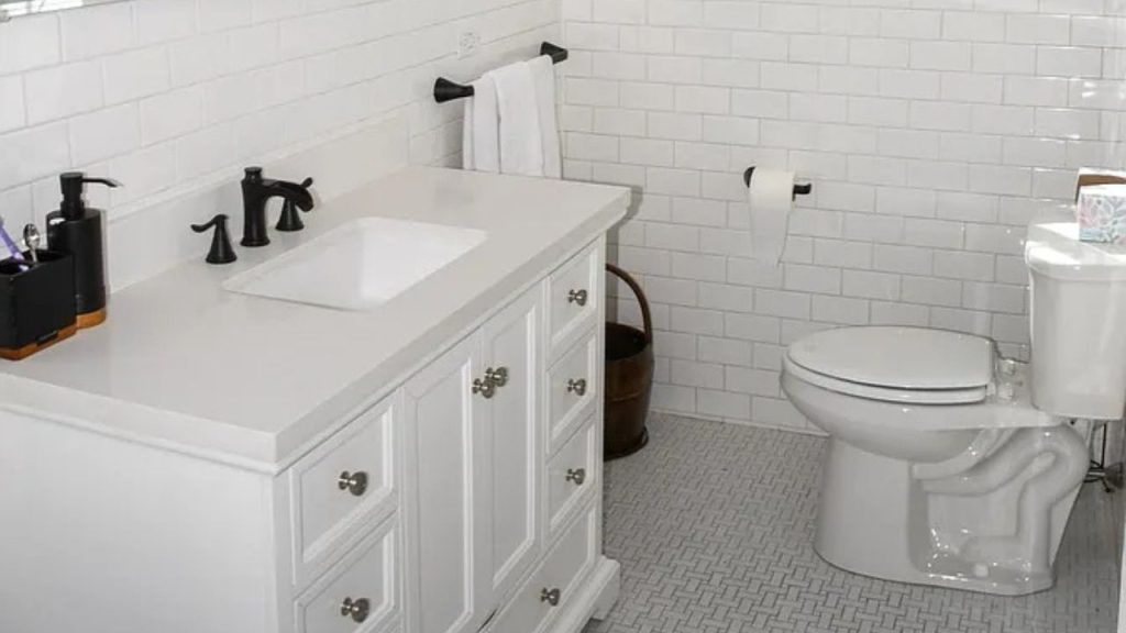 A compact bathroom with subway tile walls, a quartz vanity, and a woven basket next to the toilet.