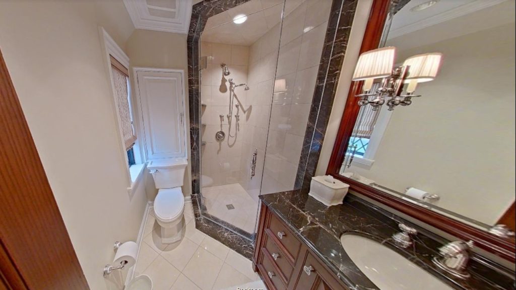 A luxurious bathroom with a glass shower, dark marble vanity, and elegant sconces, featuring tiled floors and a small window.