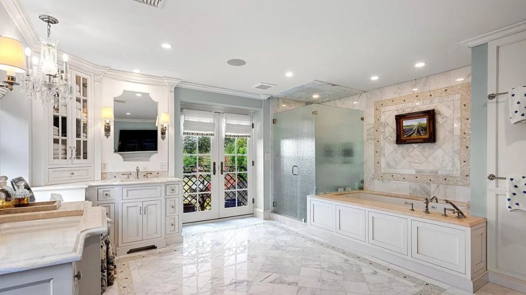 A luxurious bathroom with marble floors, a chandelier, and a garden view.