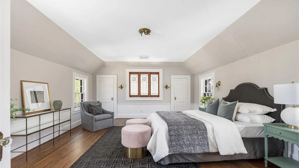 A serene bedroom with a plush bed, stained-glass windows, and pink ottomans.