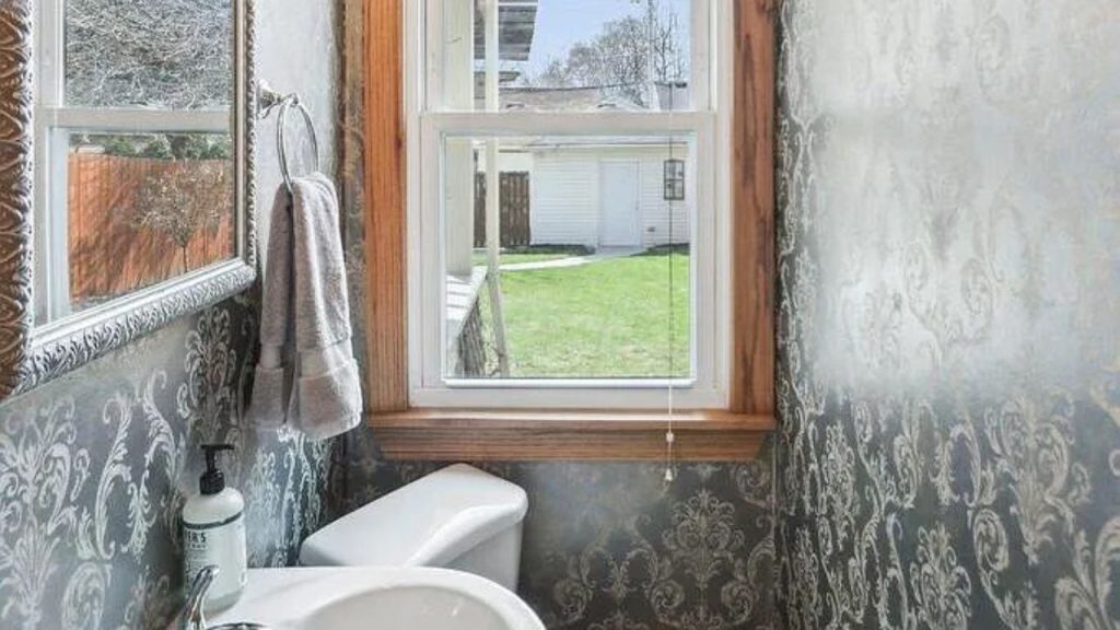 An elegant bathroom with damask wallpaper, a large window, and a white toilet.