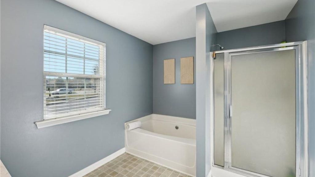 A serene bathroom with blue walls, a soaking tub, large window, and glass shower.