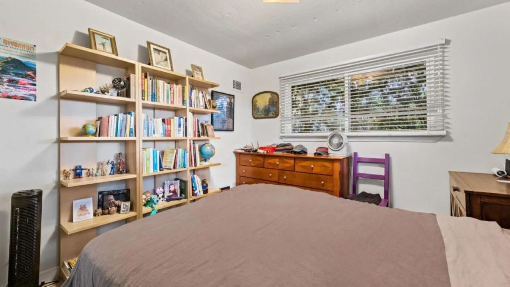 A relaxing bedroom with a wooden bed, dresser, and bookshelf by large windows.