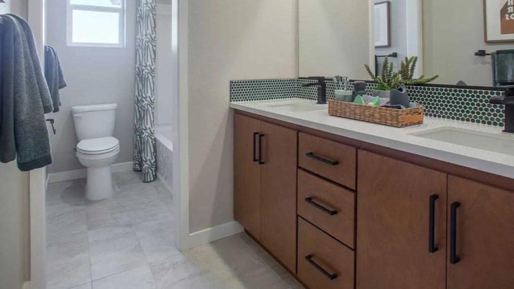 A stylish guest bathroom with a double wooden vanity, green mosaic backsplash, and a patterned shower curtain.