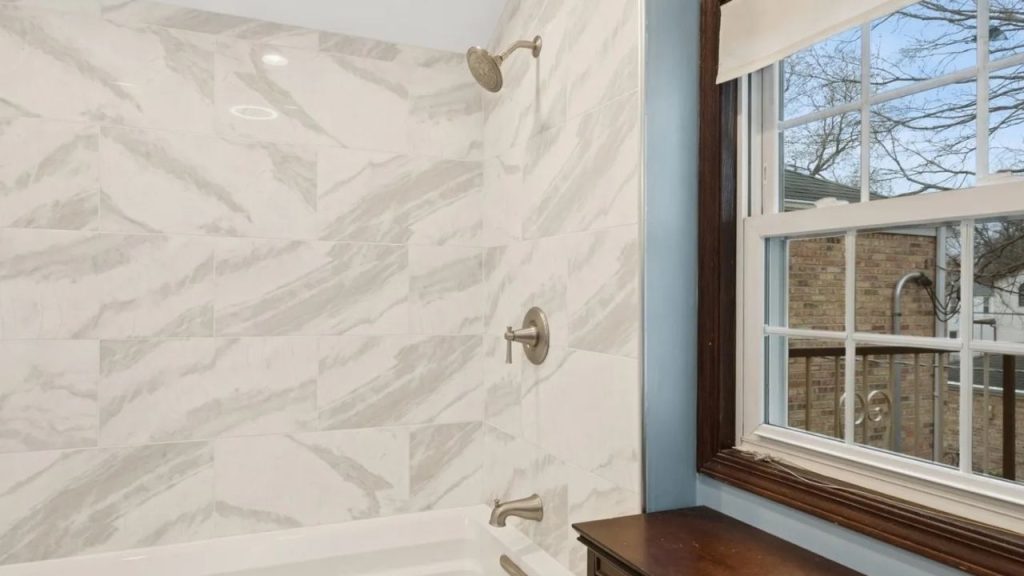 Marble-tiled shower with window and silver fixtures.