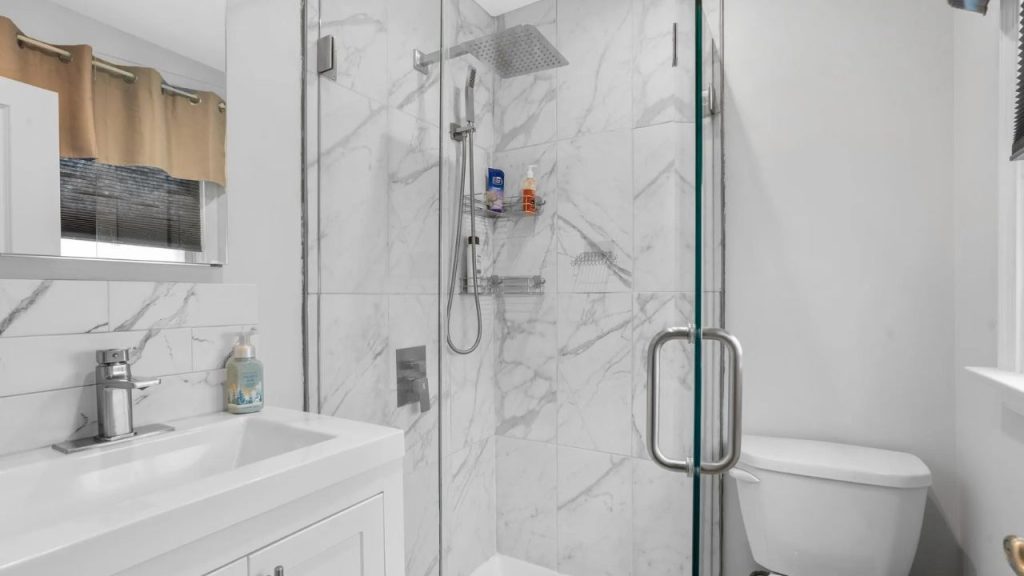 Marble-tiled shower with rainfall head, glass doors, and modern white vanity.