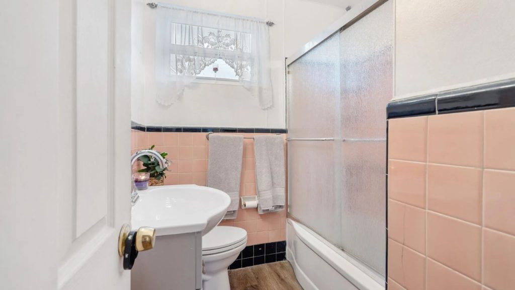 Small bathroom with pink and black tile, pedestal sink, and glass shower doors.